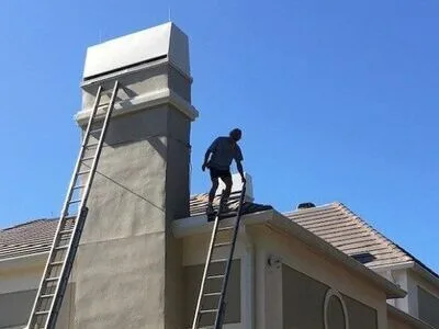 Technician on rooftop inspecting stucco chimney with extension ladder in Lakeland